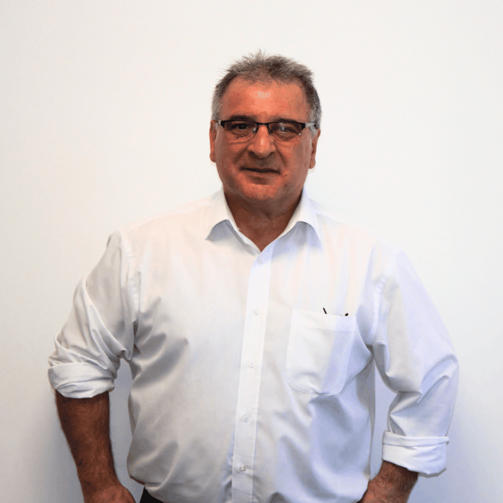 Man in a white shirt smiles, standing against a plain white background, exuding a friendly and approachable demeanor.