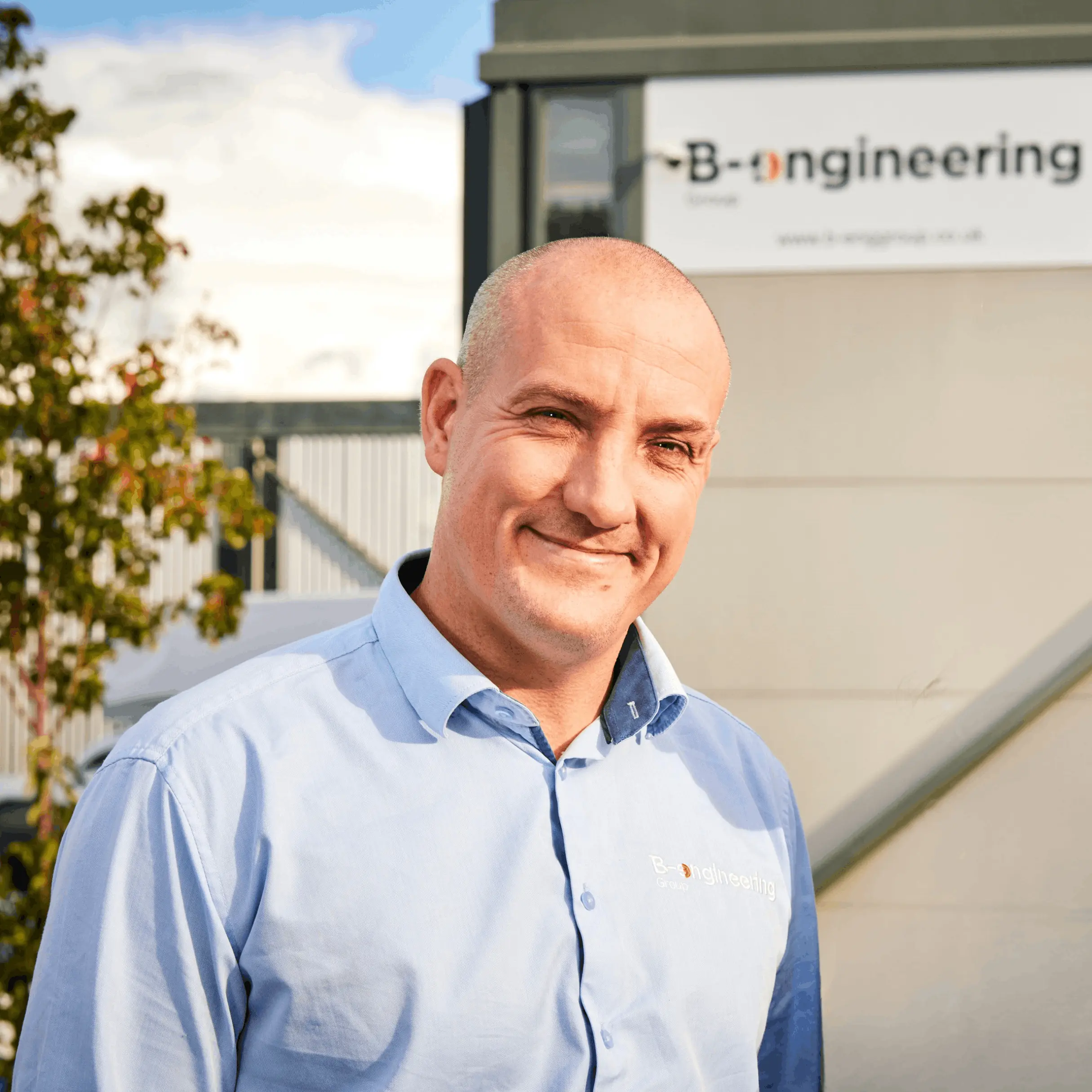 A man in a blue shirt stands infront of a building