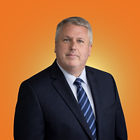 Man in a black polo shirt stands against a plain light-grey background, looking directly at the camera with a neutral expression.