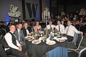A group of 7 sit around a dinner table for a black tie event
