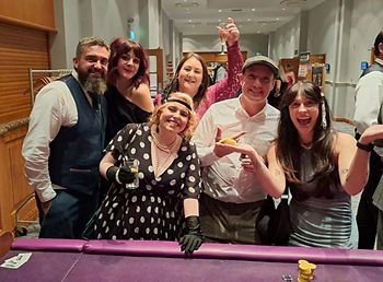 A group of people stand at the end of a poker table dressed in 1920 clothes 