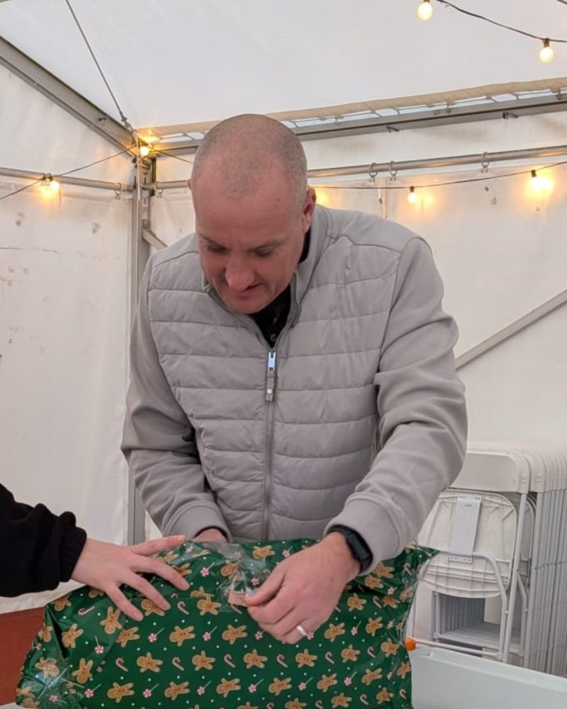 A man in a gray coat wraps a green present