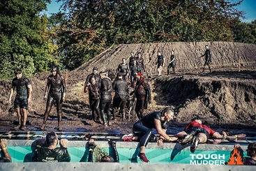 A muddy hill sees people running their way down. There is a revolving ramp that people are turning to access the other side.