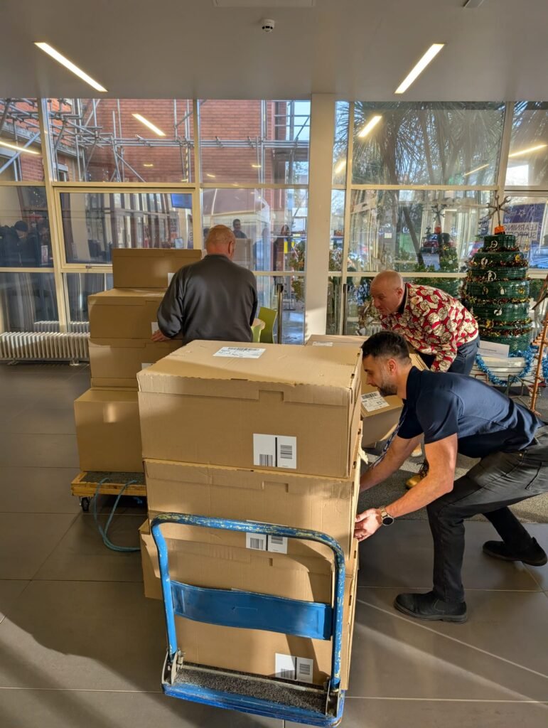 Large boxes are pilled on a dolly and are pushed by 2 men