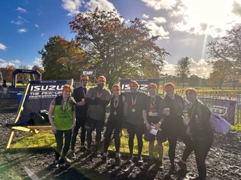 Tema of 8 stamding next to a extra large beach chair. They all have orange sweat bands and medals around their necks. 
