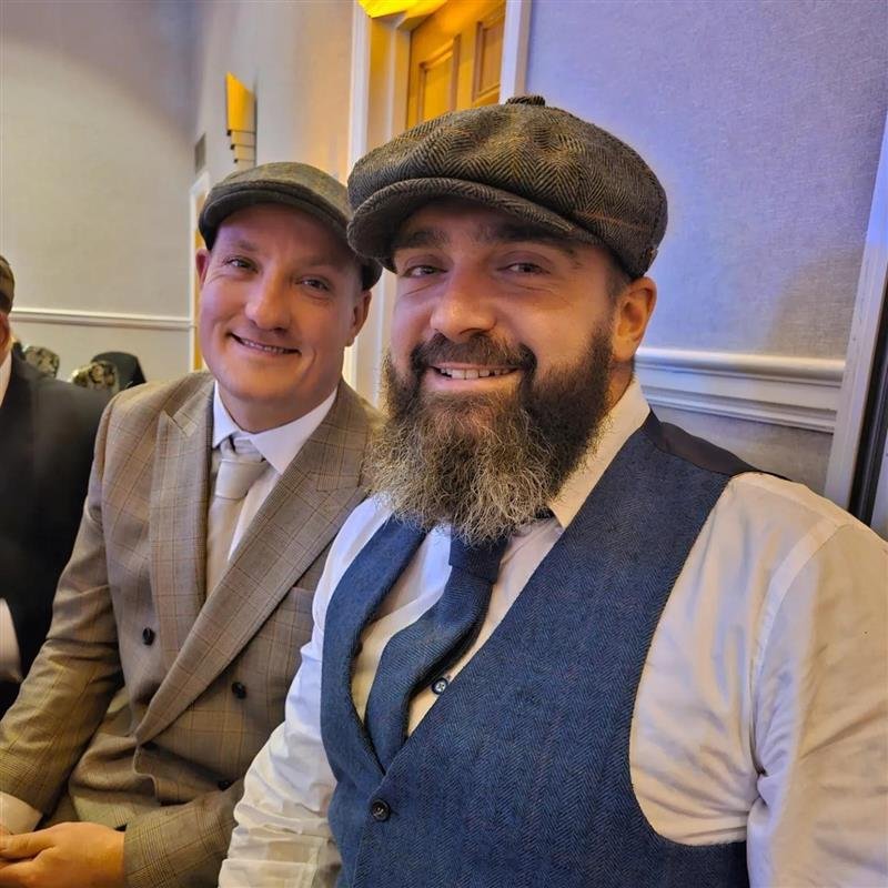 Two men dressed in 1920's attire sit facing the camera