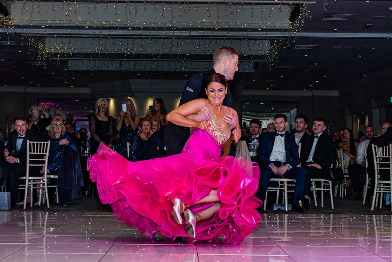 two ball room dancers dancing the quick step. The woman in the pink dress is being spun by her partner